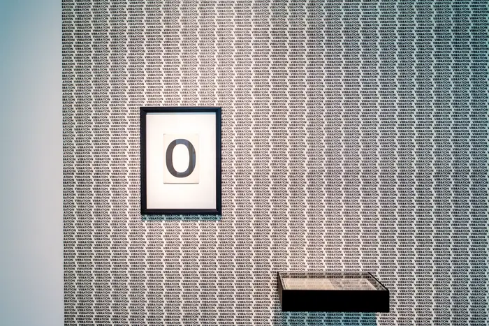 Auf einer Wand hängt ein Bild in einem schwarzen Rahmen und zeigt eine Null. 