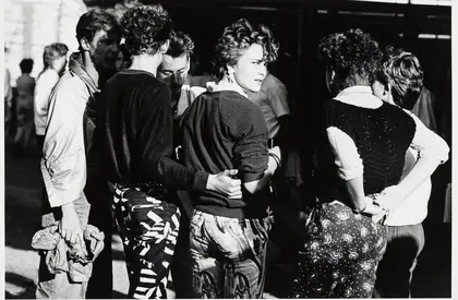 Schwarz-Weiß-Fotografie einer Gruppe, die mit den Rücken zum Betrachter steht, nur eine Frau blickt über die Schulter.
