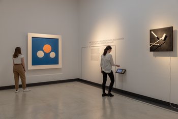 zwei Personen betrachten zwei an der Wand hängende Kunstwerke